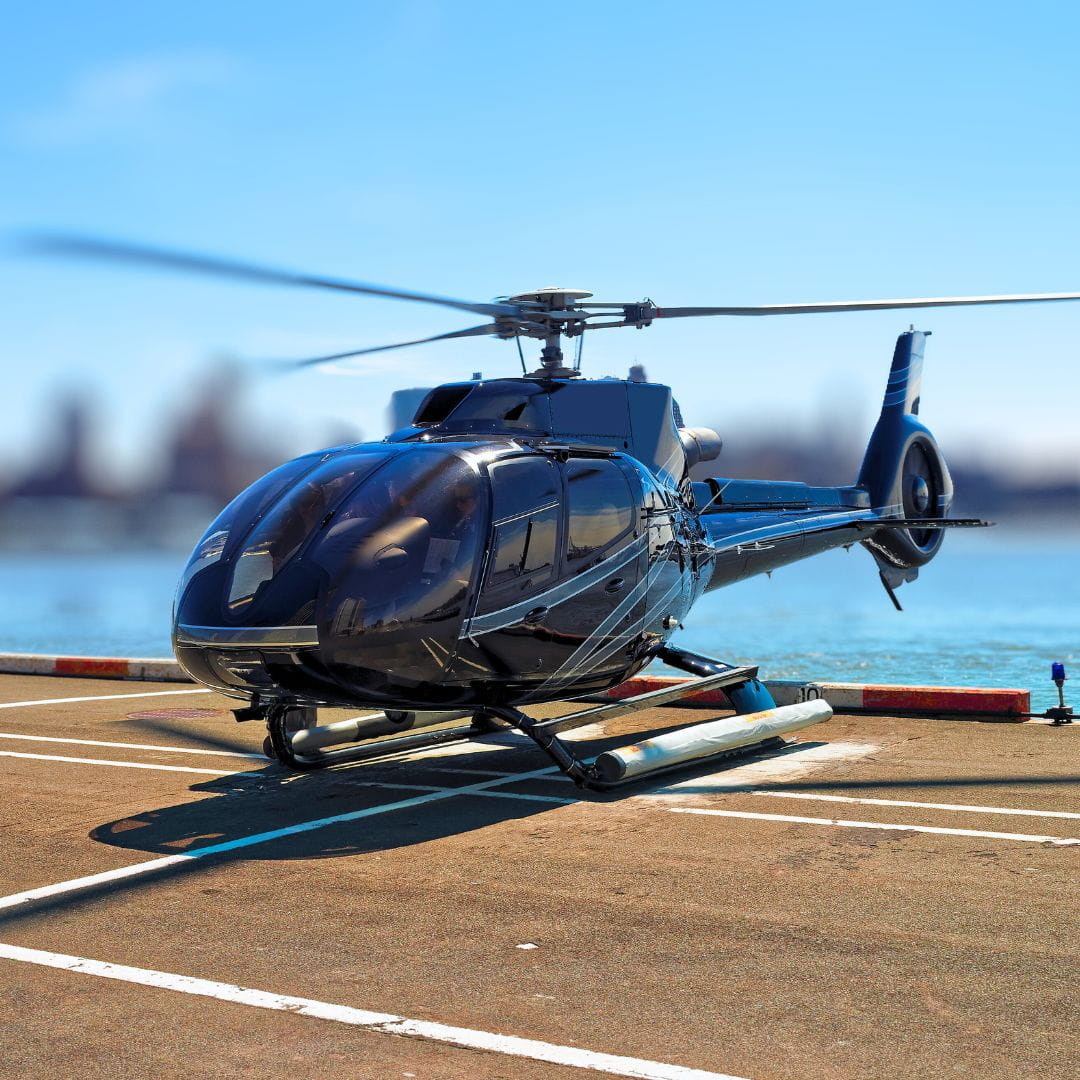 Helicopter on a waterside helipad with New York City skyline in the background, ready for a city transfer.